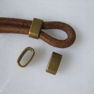 May include: Three antique brass metal cord ends for leather cord. The cord ends are oval shaped with a hole in the center.