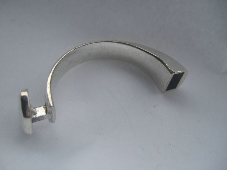 May include: A silver ring with a square-shaped opening on one end and a rounded, flat surface on the other end.