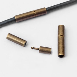 May include: Four antique gold metal cord ends for leather or fabric cords. The cord ends are cylindrical and have a smooth finish. Two of the cord ends are longer than the other two.