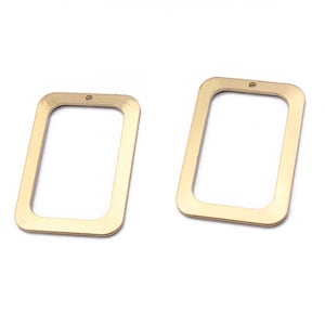 Op de afbeelding: Twee rechthoekige metalen frames in goudkleur met een klein gaatje bovenaan. De frames zijn leeg en hebben een gladde, gepolijste afwerking.