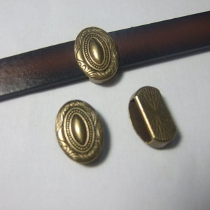 May include: Three gold-toned metal belt buckles with ornate designs. The buckles are oval-shaped with a raised centre and intricate details around the edges.