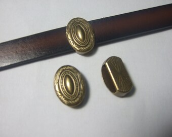 Könnte beinhalten: Drei goldfarbene Metall-Gürtelschnallen mit verzierten Designs. Die Schnallen sind oval geformt mit einer erhabenen Mitte und filigranen Details an den Rändern.