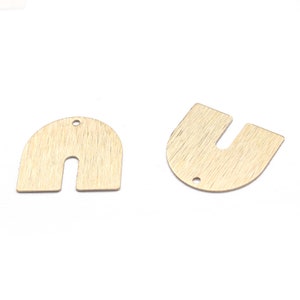 Puede incluir: Dos abalorios de metal de color dorado en forma de arco con un agujero en la parte superior. Los abalorios tienen una superficie texturizada y un recorte en forma de U.