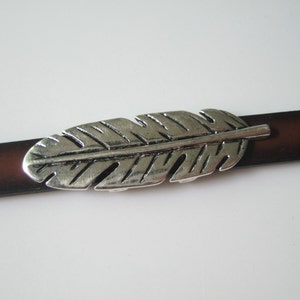 May include: A silver feather charm on a brown leather strap.