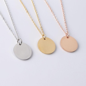 Puede incluir: Tres collares con colgantes ovalados. Los collares son plateados, dorados y oro rosa. Cada colgante cuelga de una cadena delicada. Los colgantes tienen una superficie lisa y reflectante, con un diseño minimalista.