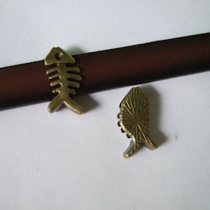 May include: Two gold-toned metal charms in the shape of fish. One charm is a stylised fish skeleton, the other is a more traditional fish shape.