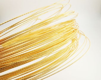 May include: A close-up of a spool of gold-colored wire with a textured surface. The wire is wound in a spiral shape.