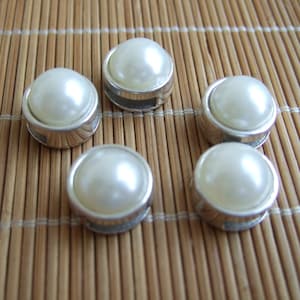 May include: Five white pearl buttons with silver settings. The buttons are arranged in a semi-circle on a bamboo surface.
