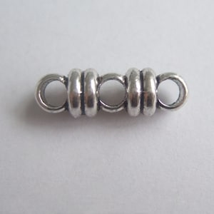 May include: Silver-toned metal connector with three round, decorative rings. The connector has two loops on either end for attaching to jewelry or other crafts.