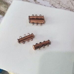 May include: Three copper-colored metal clasps with four loops each. The clasps are designed to be used as connectors for jewelry making.