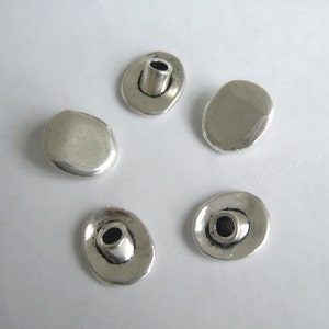 Può includere: Cinque bottoni in metallo argentato con un foro al centro. I bottoni sono di forma ovale e hanno una finitura liscia e lucida.