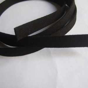 Puede incluir: Cordón de cuero de ante negro, de aproximadamente 6 mm de ancho, enrollado sobre una superficie blanca.