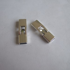 May include: Two silver-toned metal clasps for jewelry making. The clasps are rectangular with a small opening in the center.