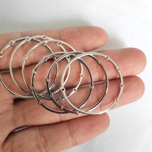 Puede incluir: Cinco anillos de metal plateado con pequeños agujeros alrededor de los bordes. Los anillos están apilados uno encima del otro.