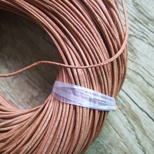 Puede incluir: Primer plano de un carrete de cordón de cuero marrón. El cordón está enrollado apretado y está asegurado con una banda de plástico transparente.