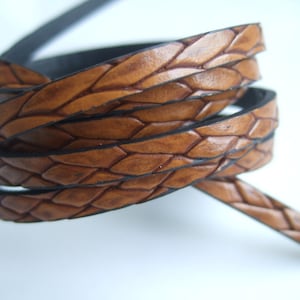 May include: A close-up of a brown leather cord with a braided design. The cord is woven with a diamond pattern and has a dark brown edge.