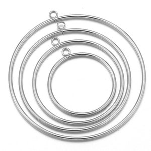 May include: Set of four silver metal hoops with jump rings. The hoops are nested inside each other, with the largest hoop at the bottom and the smallest hoop at the top.
