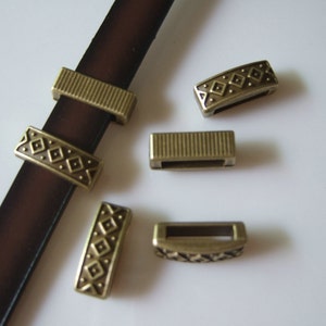 May include: Five antique gold-toned metal belt buckle slides with a geometric design. The slides are rectangular and have a small opening in the center.