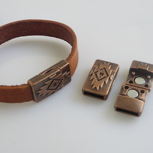 May include: A brown leather bracelet with a copper-toned magnetic clasp. The clasp features a geometric design.