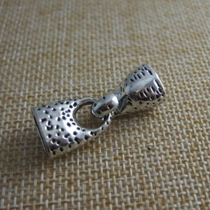 May include: Silver metal cord end with a textured finish. The end has a loop and a small, round, textured cap.