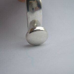 May include: A silver ring with a round, flat top. The ring is made of smooth, polished metal.