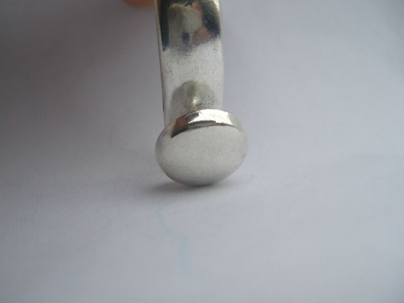 May include: A silver ring with a round, flat top. The ring is made of smooth, polished metal.