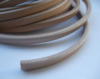 May include: Close-up of a roll of light brown leather cord with a textured edge.