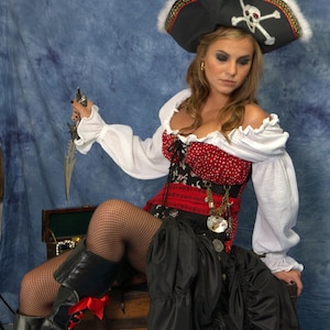 May include: A pirate costume featuring a black hat with a skull and crossbones, a red and white bodice, a black skirt, and black boots. The pirate is holding a dagger. The costume includes a white blouse and fishnet stockings.