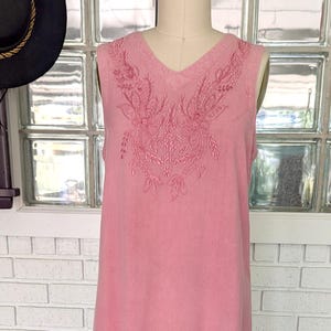 May include: A sleeveless, pink dress with intricate embroidered detailing on the bodice and hem. The dress features a V-neck and a layered, scalloped hemline. The dress is displayed on a mannequin.