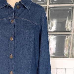 May include: A long-sleeved denim dress with a button-up front and a collared neckline. The dress is a dark blue color and has a slightly flared skirt.