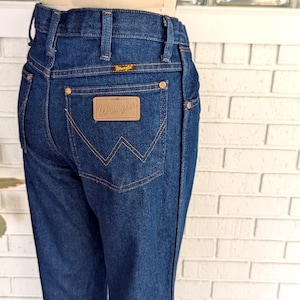 K&ouml;nnte beinhalten: Eine dunkelblaue Jeanshose mit einem braunen Leder-Patch auf der Ges&auml;&szlig;tasche, auf dem "Wrangler" steht.