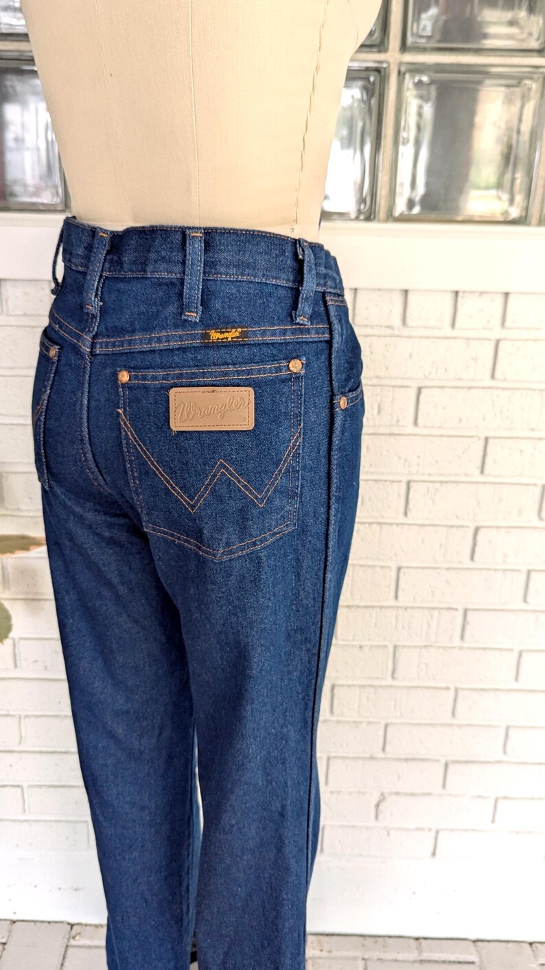 K&ouml;nnte beinhalten: Eine dunkelblaue Jeanshose mit einem braunen Leder-Patch auf der Ges&auml;&szlig;tasche, auf dem "Wrangler" steht.