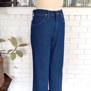 K&ouml;nnte beinhalten: Eine dunkelblaue Jeanshose mit hoher Taille und weitem Bein. Die Jeans befindet sich auf einem Mannequin und wird in einem Gesch&auml;ft ausgestellt.