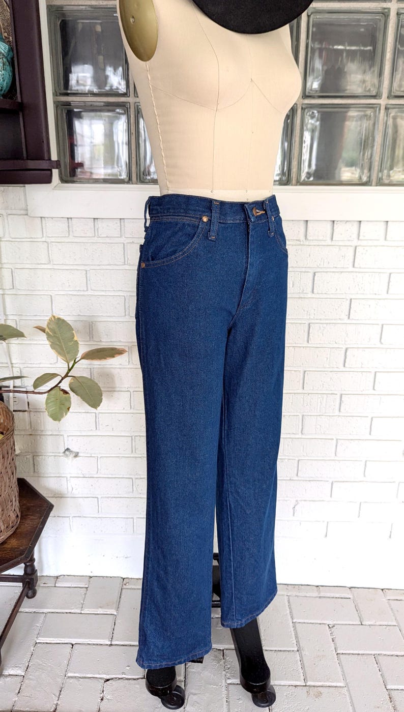 K&ouml;nnte beinhalten: Eine dunkelblaue Jeanshose mit hoher Taille und weitem Bein. Die Jeans befindet sich auf einem Mannequin und wird in einem Gesch&auml;ft ausgestellt.