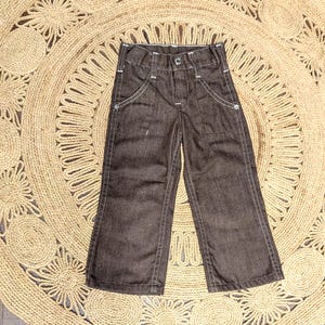 May include: Dark brown denim pants with white stitching and pockets. The pants have a button fly and belt loops.