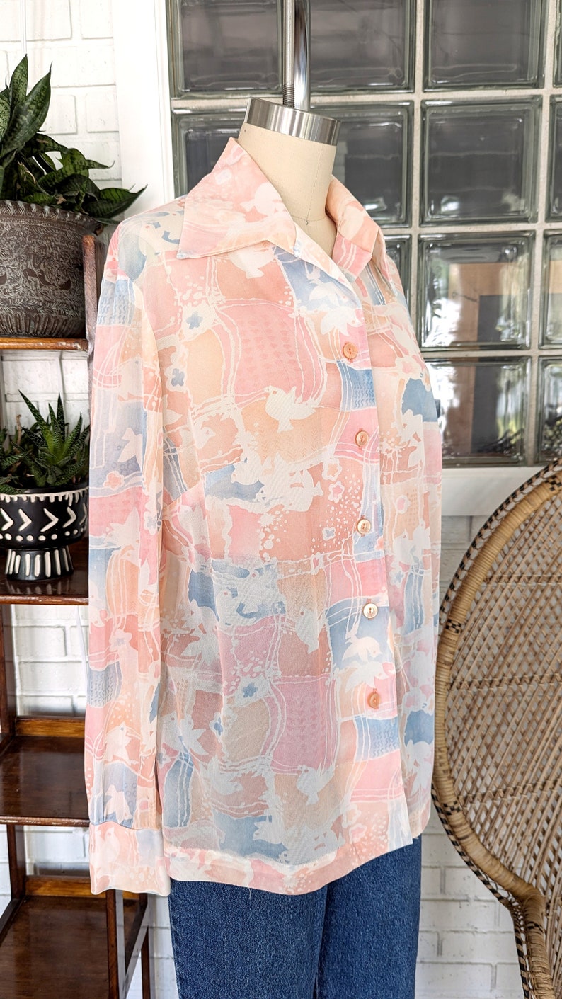Peut inclure: Une chemise &agrave; manches longues boutonn&eacute;e avec un imprim&eacute; abstrait rose, bleu et blanc. La chemise est en tissu transparent et a un col.