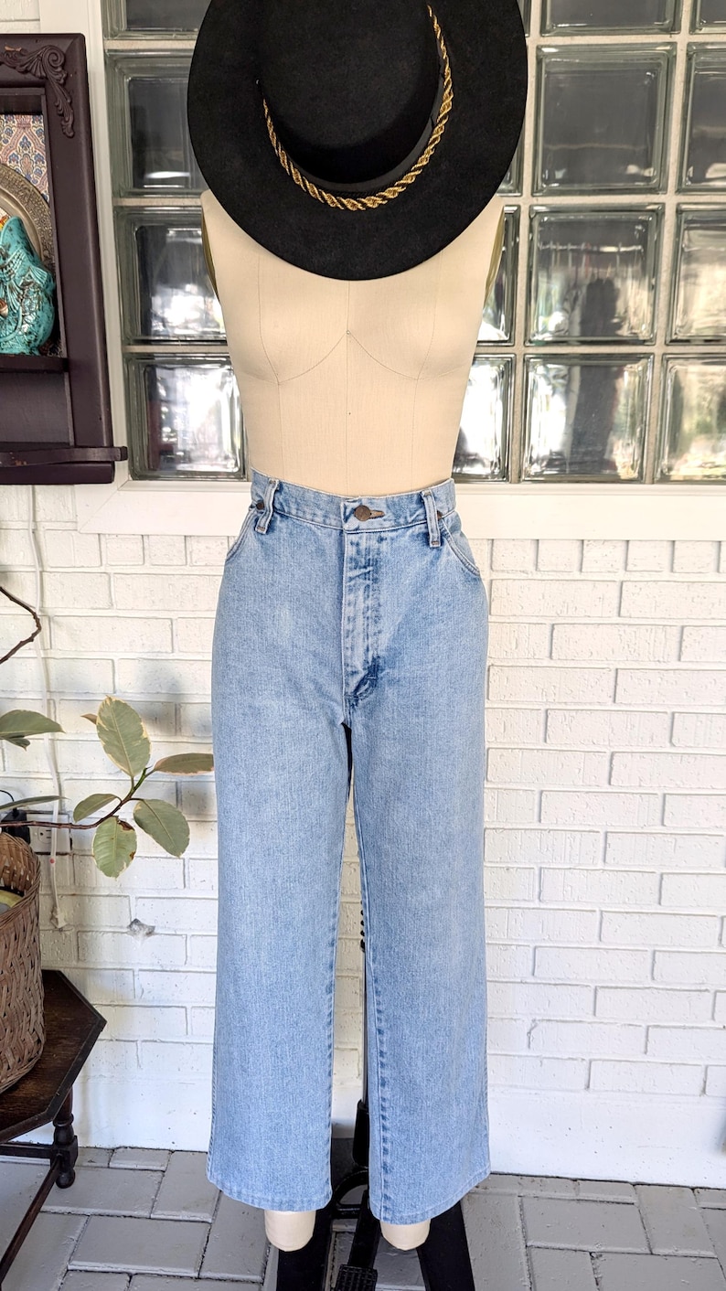 K&ouml;nnte beinhalten: Hellblaue Jeans mit hoher Taille und geradem Bein. Die Jeans befinden sich an einem Mannequin, das einen schwarzen Hut mit goldfarbenem Band tr&auml;gt.
