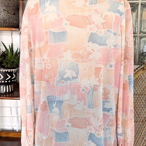 Peut inclure: Une blouse &agrave; manches longues, de couleur rose p&acirc;le, bleue et blanche &agrave; motifs, avec un col. La blouse a une coupe ample et est faite d'un tissu transparent.