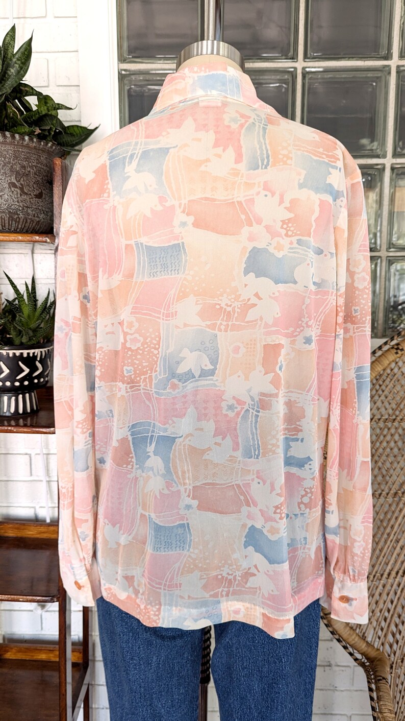 Peut inclure: Une blouse &agrave; manches longues, de couleur rose p&acirc;le, bleue et blanche &agrave; motifs, avec un col. La blouse a une coupe ample et est faite d'un tissu transparent.
