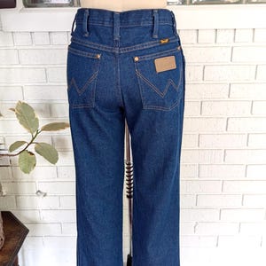 K&ouml;nnte beinhalten: Eine dunkelblaue Jeanshose mit einem braunen Leder-Patch auf der Ges&auml;&szlig;tasche, auf dem "Wrangler" steht.