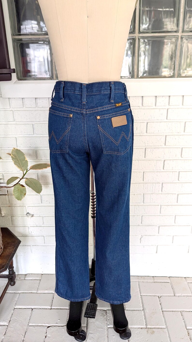 K&ouml;nnte beinhalten: Eine dunkelblaue Jeanshose mit einem braunen Leder-Patch auf der Ges&auml;&szlig;tasche, auf dem "Wrangler" steht.