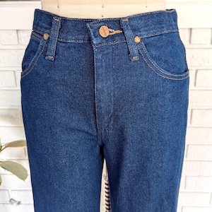 K&ouml;nnte beinhalten: Eine dunkelblaue Jeanshose mit einem braunen Leder-Patch am hinteren Bund, auf dem "Wrangler" steht.