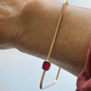 May include: A gold square bangle bracelet with a red rectangular stone set in the centre.