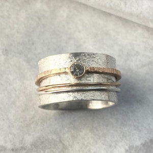 May include: A silver spinning ring with a clear gemstone and two gold bands.