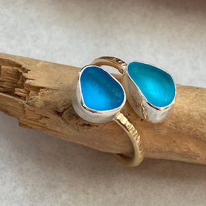 May include: A silver ring with two blue sea glass stones set in silver. The ring is on a piece of driftwood.