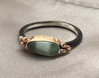May include: A silver ring with a black band and a light blue oval gemstone. The ring has small gold accents on either side of the stone.