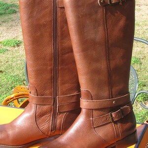 May include: A pair of brown leather knee-high boots with buckles and zippers. The boots have a low heel and a rounded toe.
