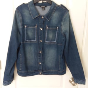 May include: A blue denim jacket with a button closure and two flap pockets on the front. The jacket has a distressed look and is made of a soft, comfortable fabric.