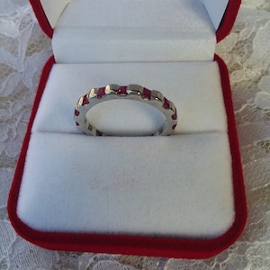 May include: A silver band ring with a row of small, square-shaped ruby red stones set into the band.