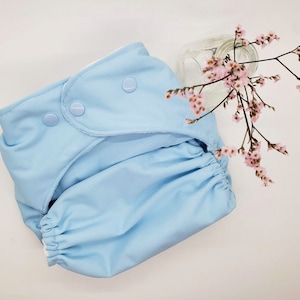 May include: A light blue reusable cloth diaper with white trim and three snap closures. The diaper is folded and laid flat on a white surface.